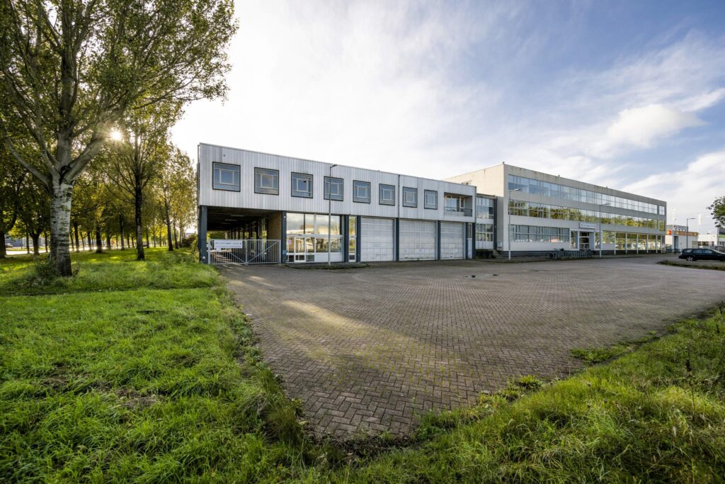 Exterior view of a commercial building at Van der Madeweg with a paved parking area and surrounding greenery.